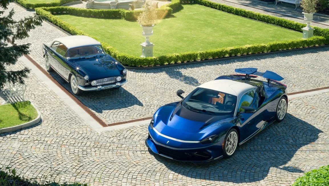 Dos automóviles estacionados en un camino empedrado; uno clásico y otro deportivo, ambos de color azul con techo blanco, rodeados de jardín bien cuidado.